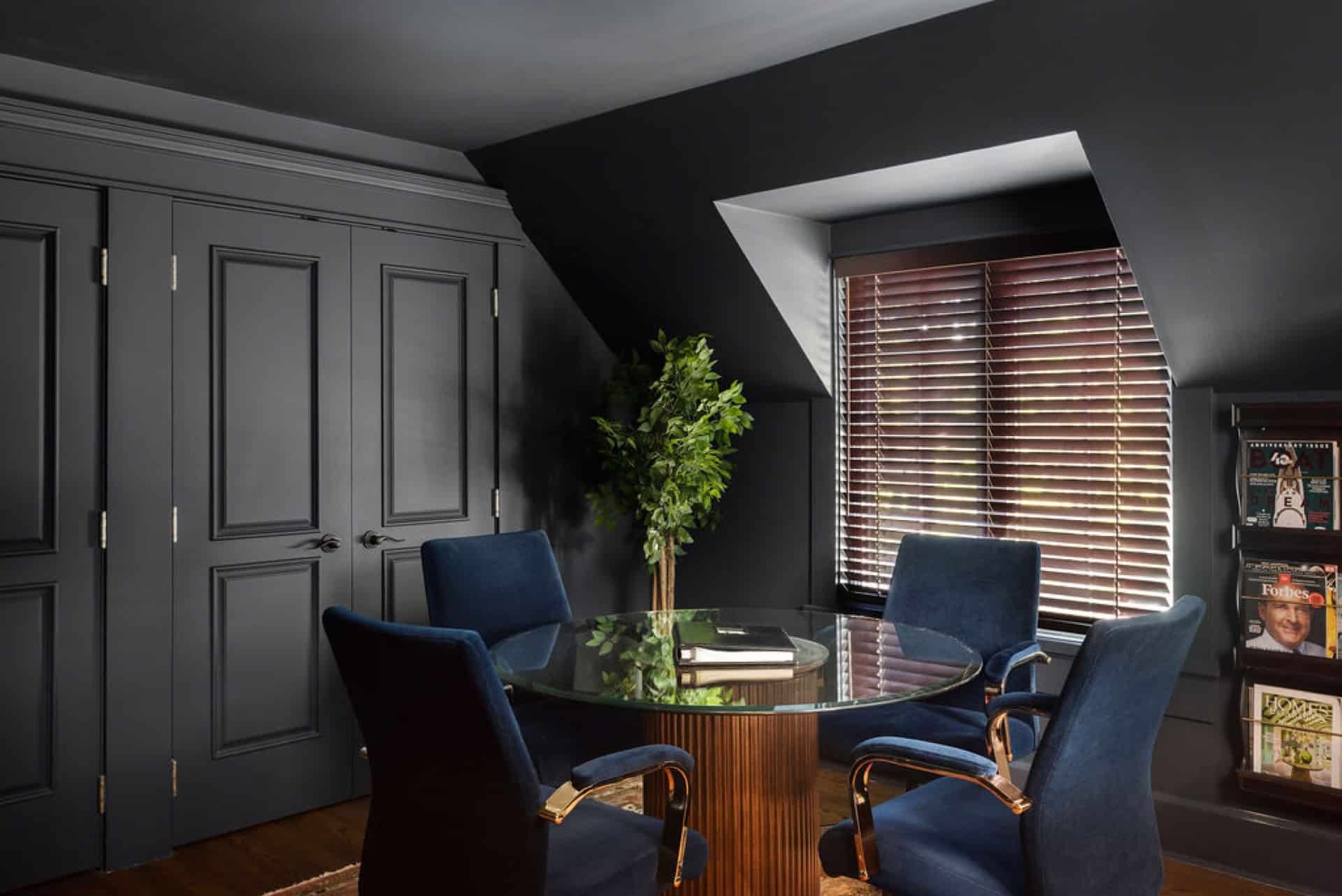 Dark modern meeting room with round glass table and blue chairs under a sloped ceiling.