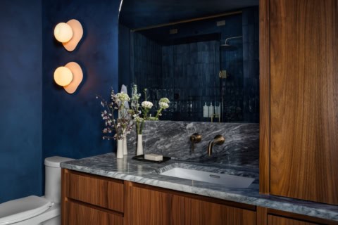 Blue bathroom with marble countertop, wooden cabinetry, and brass fixtures in a modern design.