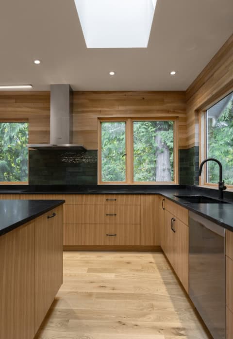 Modern kitchen with wooden cabinets, black countertops, and skylight in Victoria BC home by White_Wo.