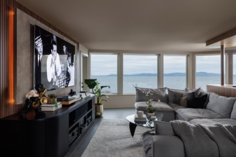 Modern living room with large windows overlooking a coastal landscape and grey sectional sofa.