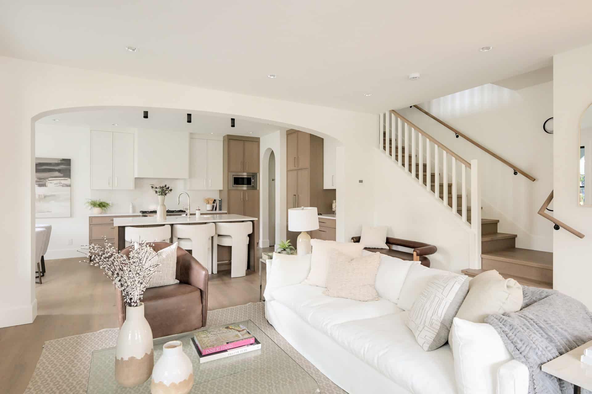 Living area of a modern home with white and neutral tones, open layout, and staircase in a Victoria,.