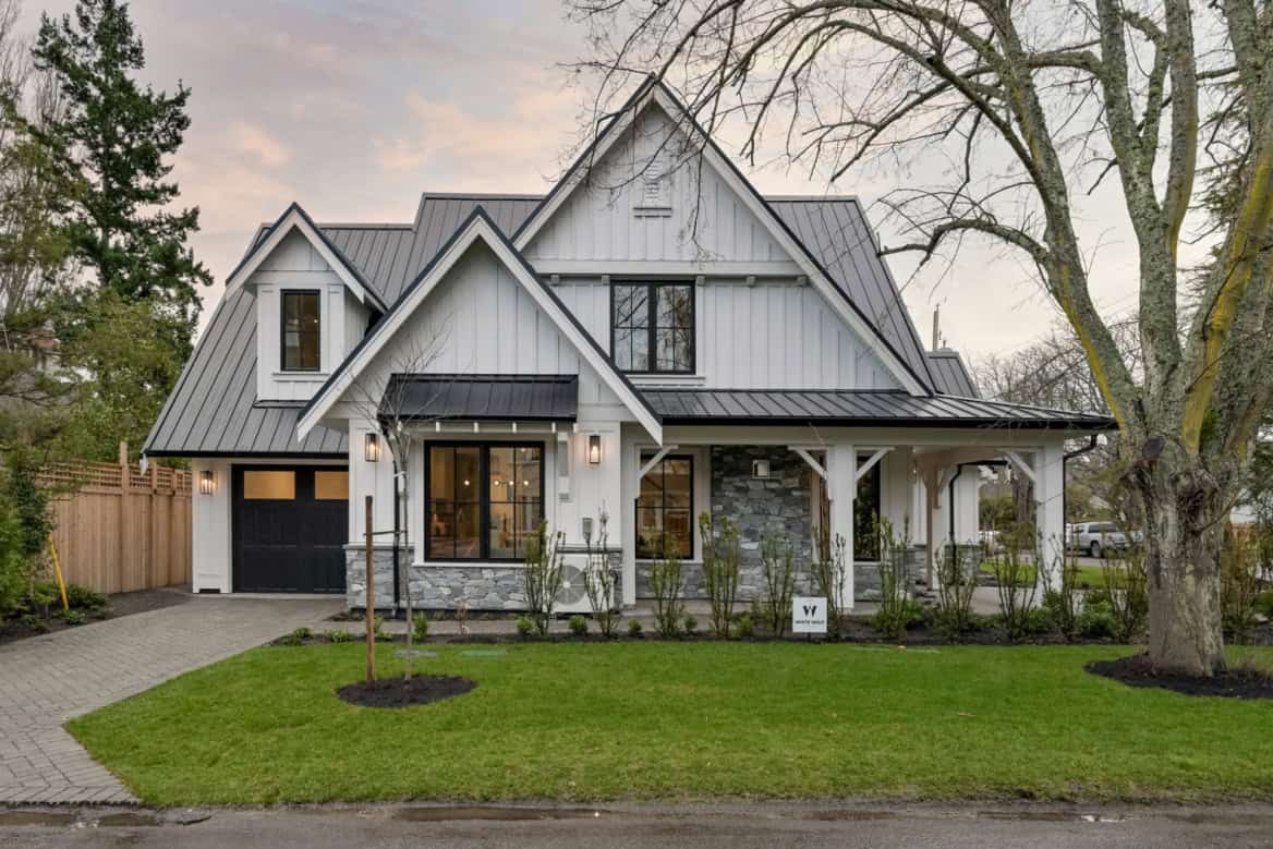 Custom Victoria BC home with white siding, gray roof, stone accents, front porch, and landscapedyard.