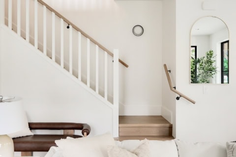 Bright interior with white walls, wooden staircase and arched mirror in a modern living space.