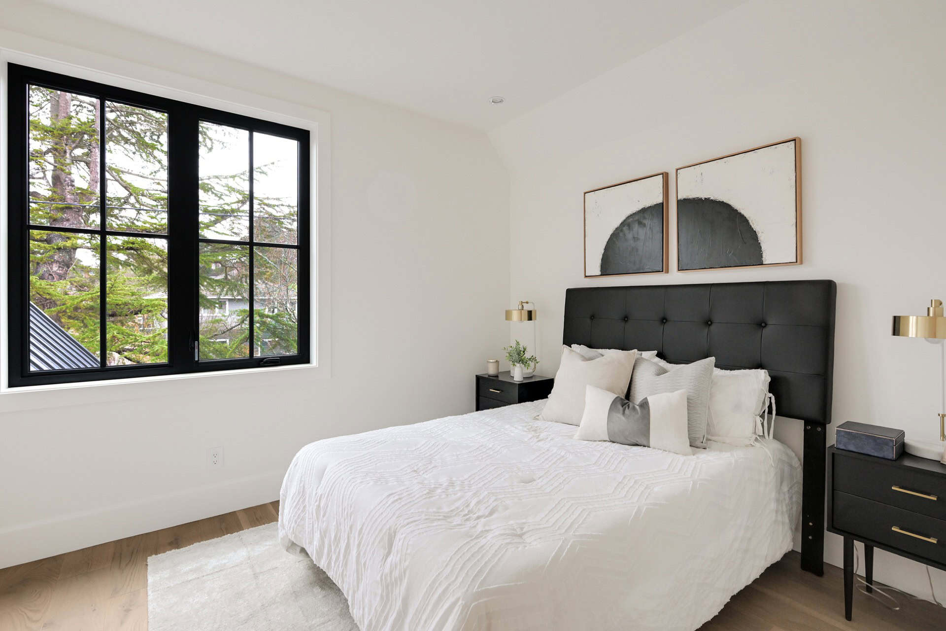 Modern bedroom featuring a black tufted headboard, white bedding, and large window overlooking trees.