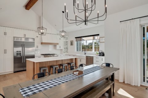 Modern open-concept kitchen with island, white cabinets, and rustic dining table.
