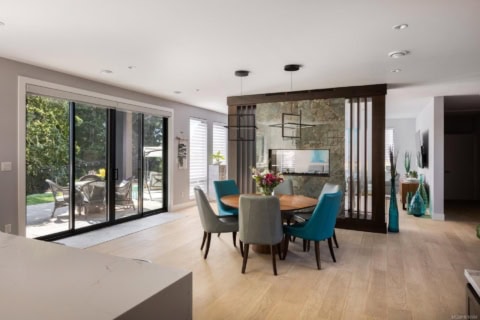 Bright dining area with glass doors opening to a patio, teal and gray chairs around a round table.
