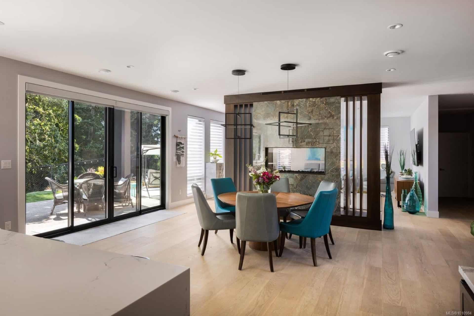 Bright dining area with glass doors opening to a patio, teal and gray chairs around a round table.