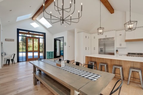 Bright modern kitchen and dining area with timber beams and a long rustic table.