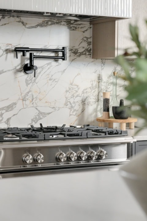 Modern kitchen stove with marble backsplash and black faucet in Cedar & Stone home by White Wolf.