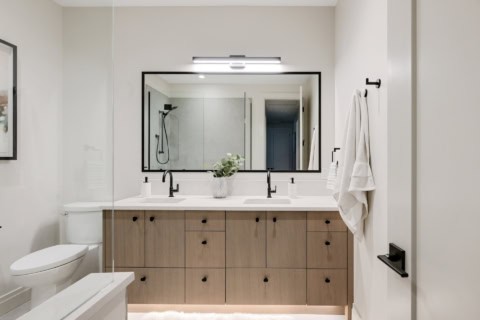 Modern bathroom with double vanity, wood cabinetry, glass shower enclosure and large mirror.