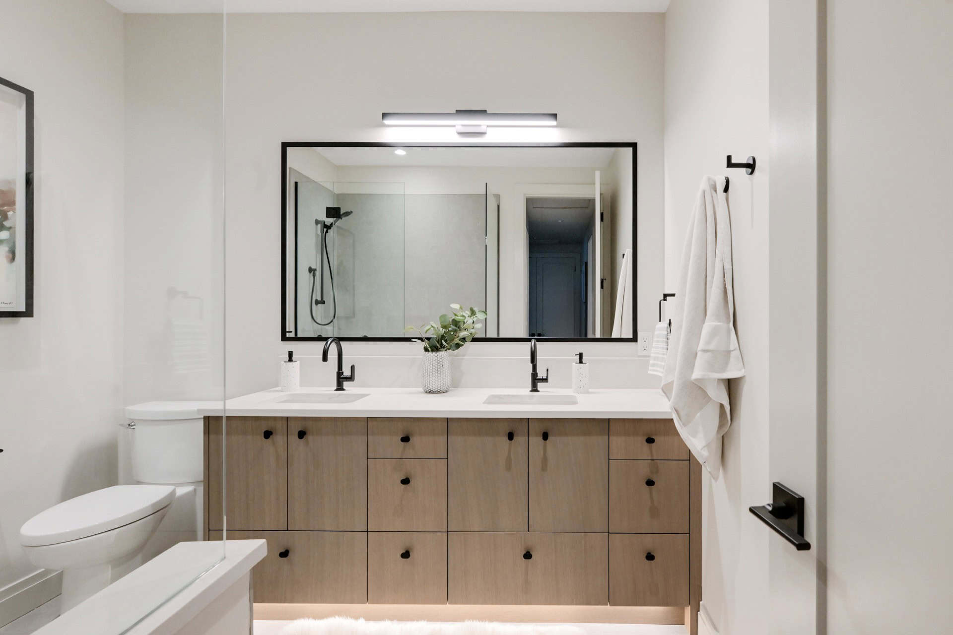 Modern bathroom with double vanity, wood cabinetry, glass shower enclosure and large mirror.