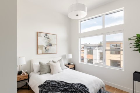 Bright modern bedroom with white bedding, large window, and minimalist decor in Arbor Hill project.