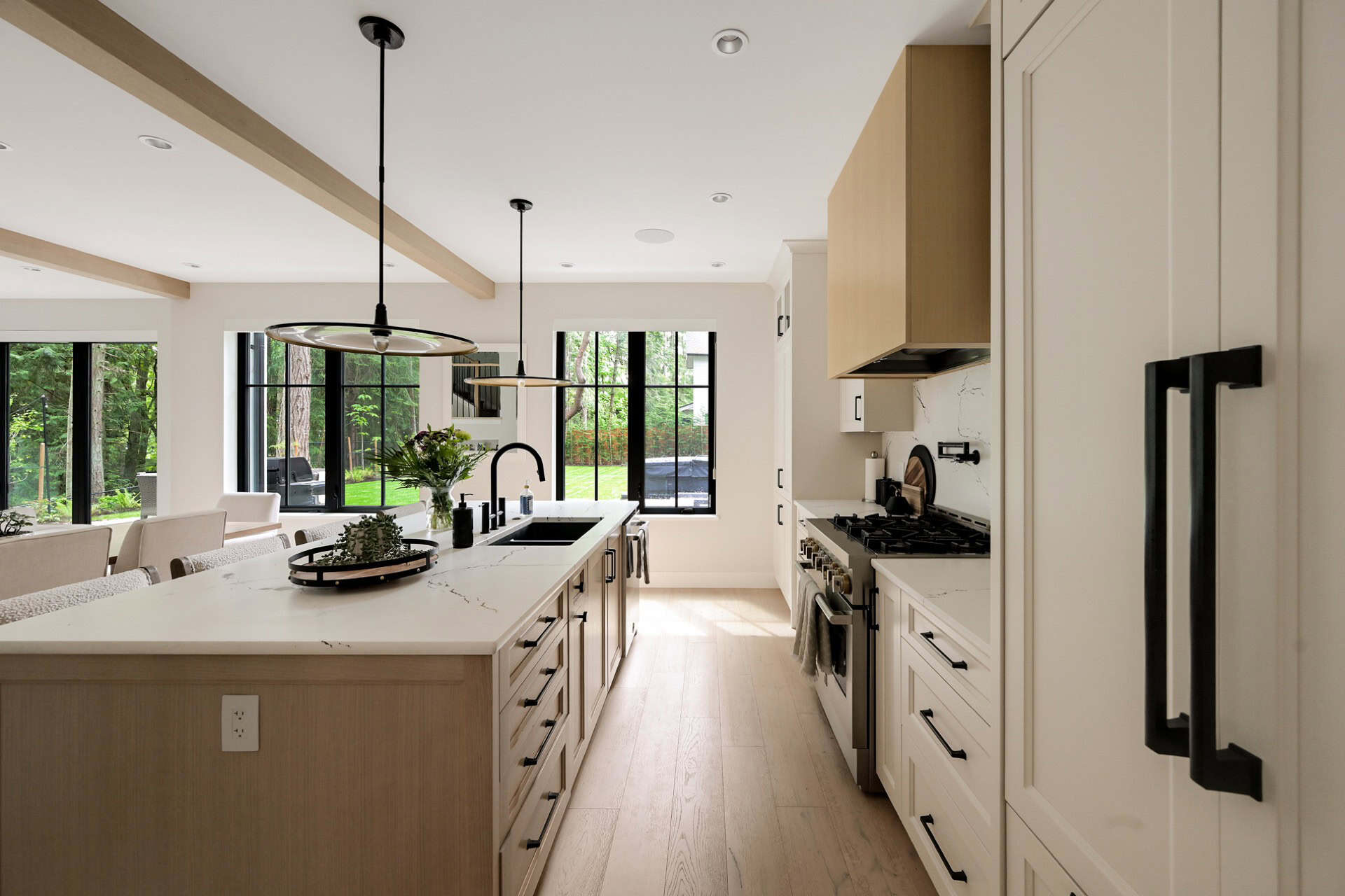 Modern white kitchen with island, pendant lights, and stainless steel appliances in Victoria BC home.