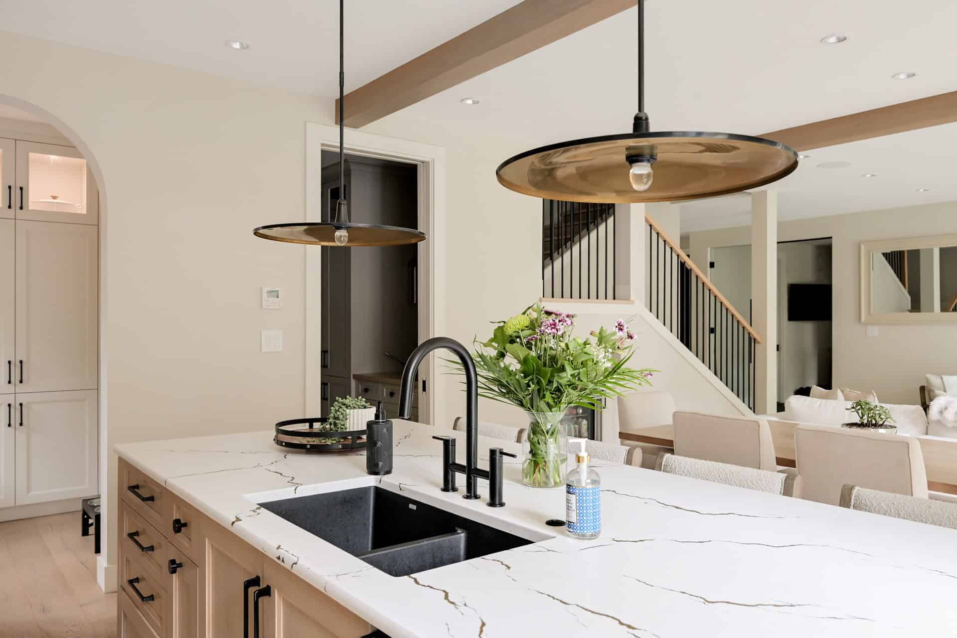 Modern kitchen island with marble countertop, black sink, pendant lights, and open living area.