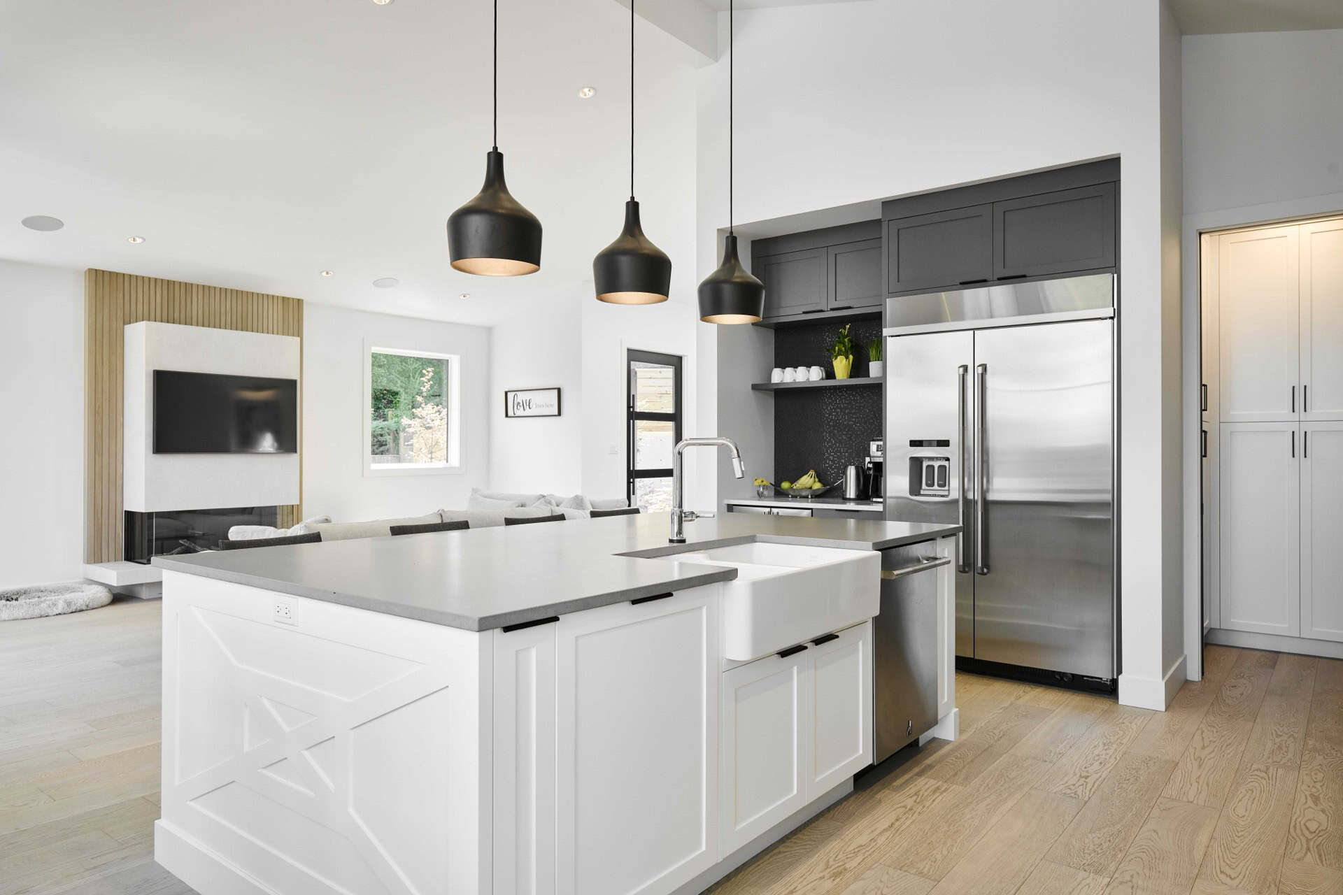 Modern white kitchen with island, pendant lights, and stainless steel appliances.