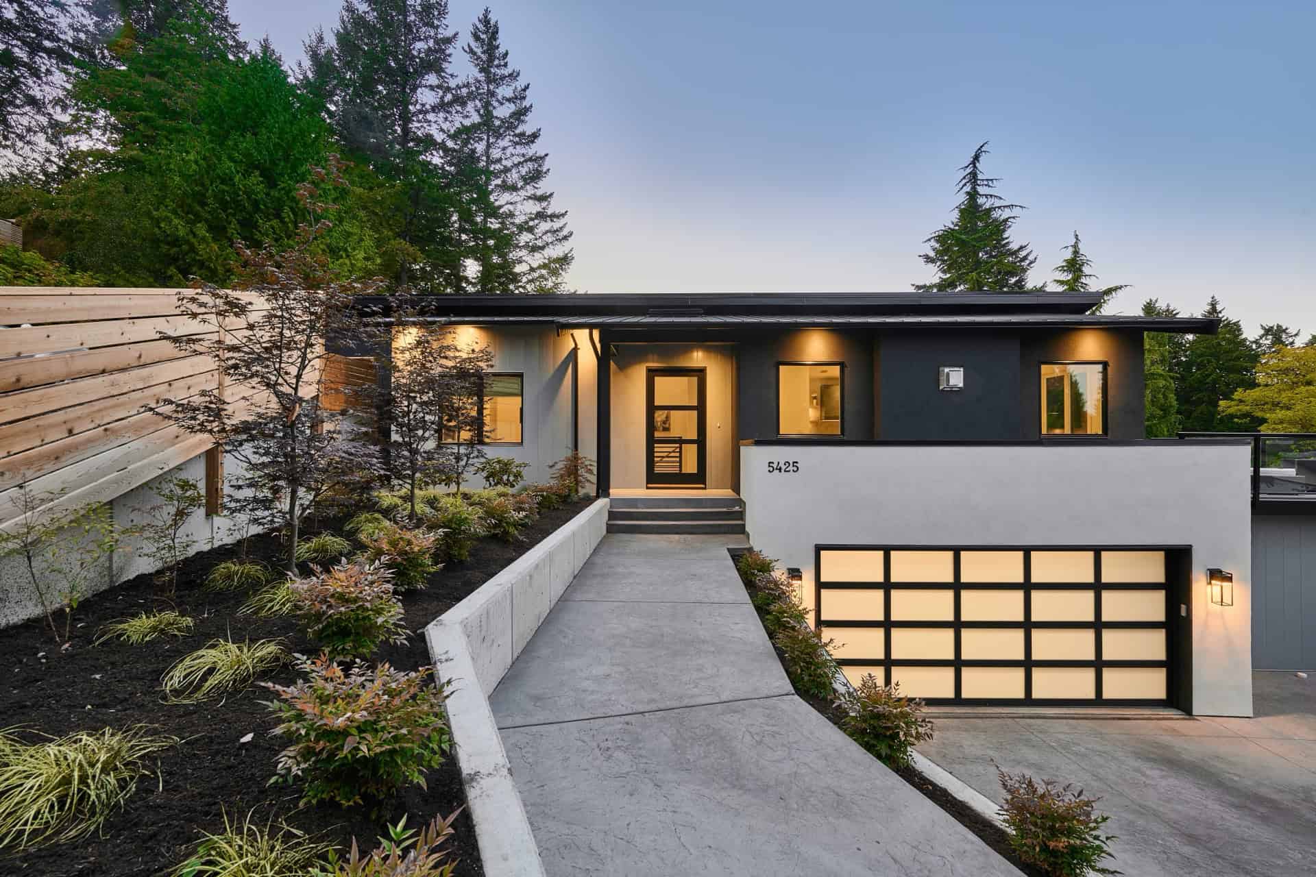 Grey and black modern duplex style home with landscaped path to entrance and a two-car garage.