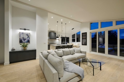 Bright modern living area with beige sectional sofa, glass coffee table, and open kitchen.