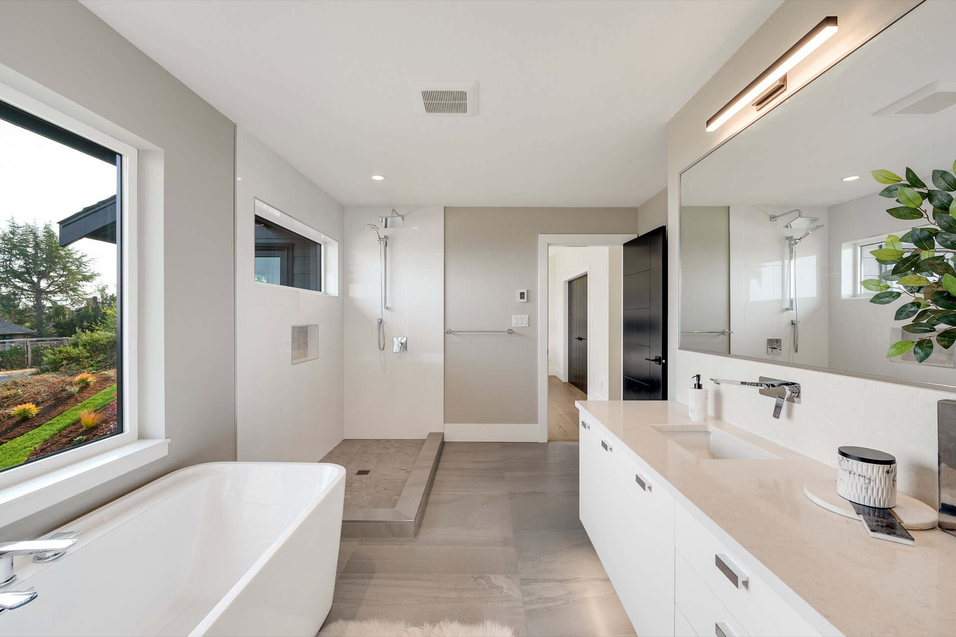 Bright modern bathroom with freestanding tub, double vanity, and large window.