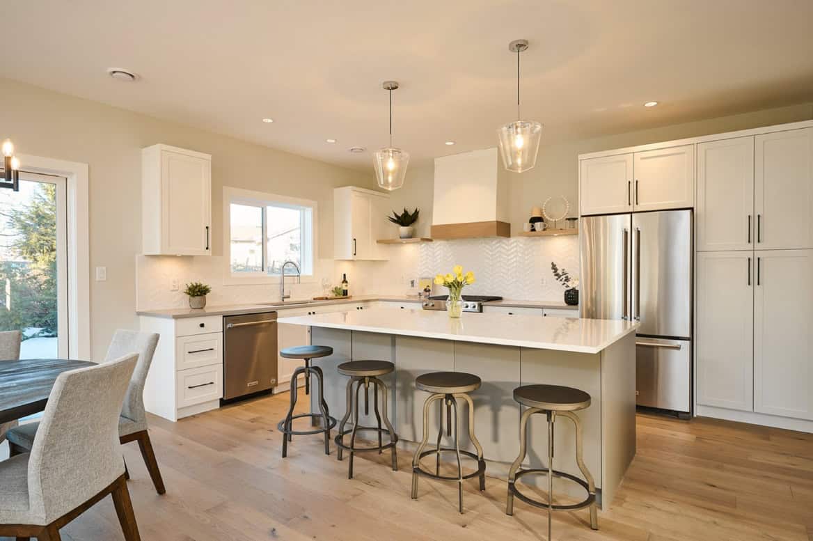 Modern white kitchen with island, pendant lights, and stainless appliances in Meadowview home by a B.