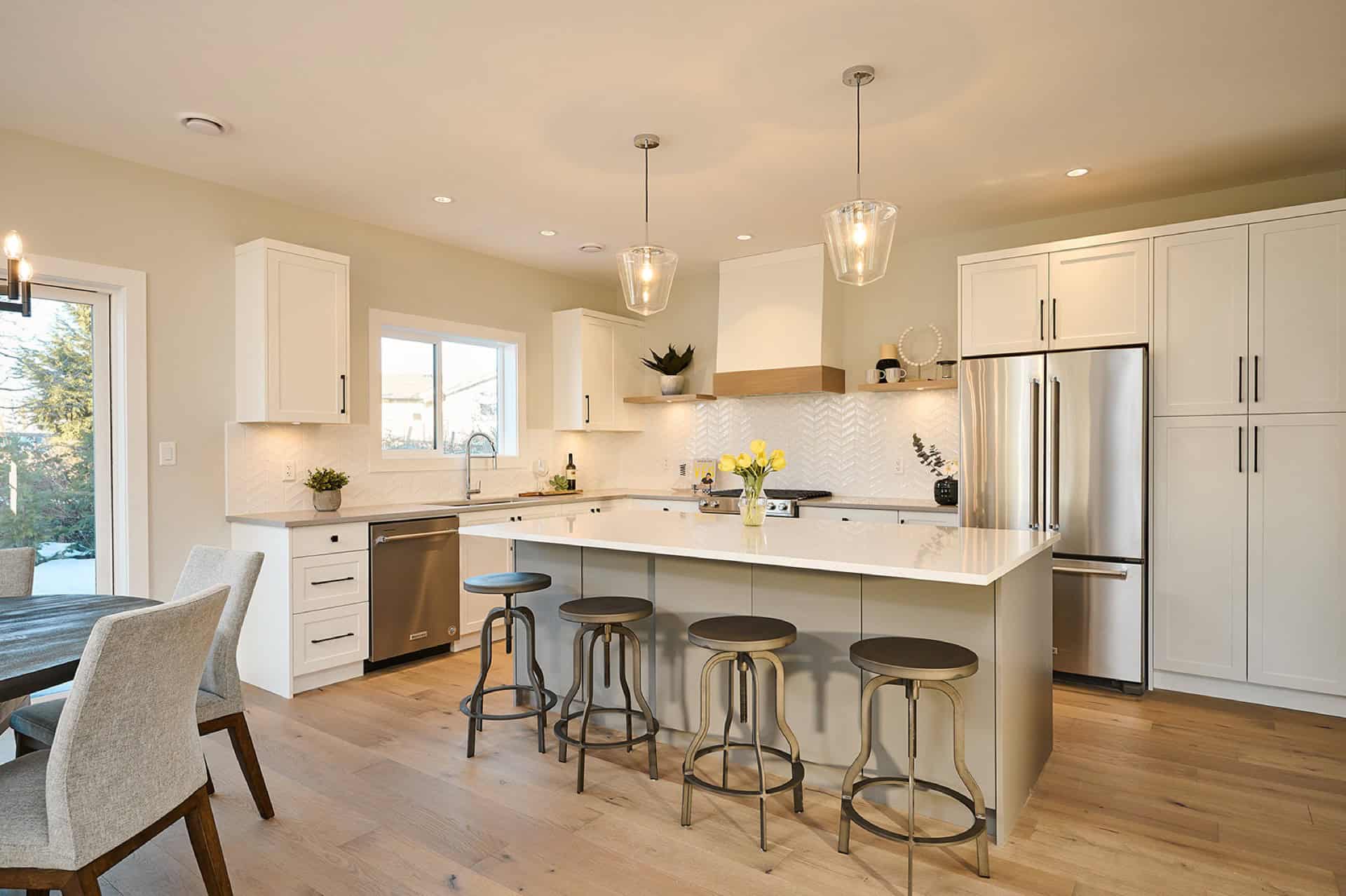 Modern white kitchen with island, pendant lights, and stainless appliances in Meadowview home by a B.