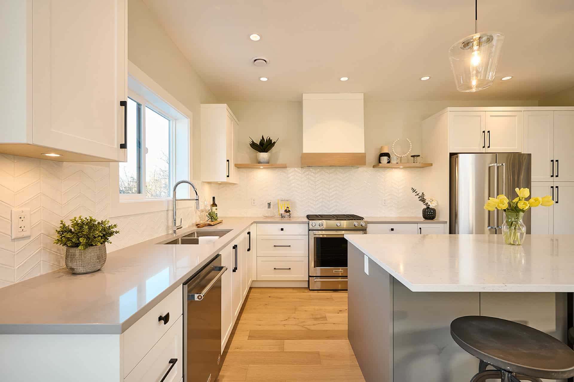 Modern white kitchen with island, stainless steel appliances and light wood floors.