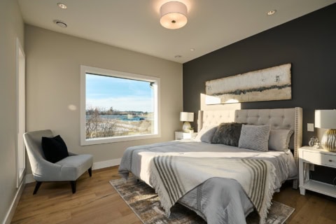 Modern master bedroom with large window, neutral tones, and upholstered headboard.