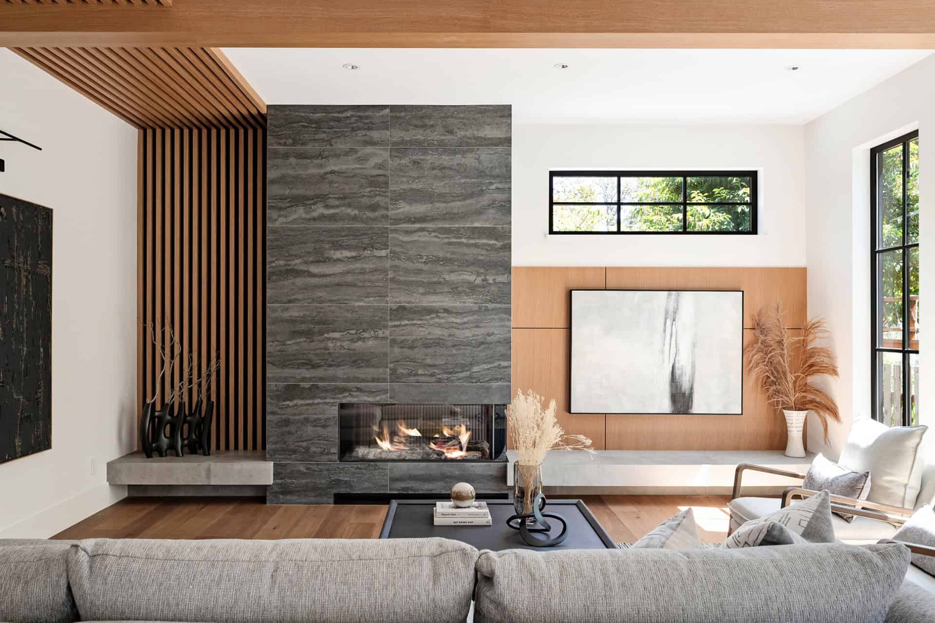 Modern living room with gray stone fireplace, wood accents, and large windows.