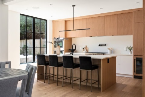 Modern kitchen with island, wooden cabinetry and black bar stools.