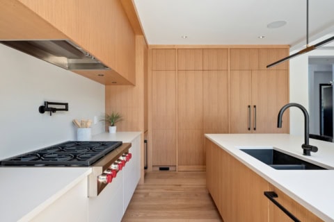 Modern kitchen with light wood cabinets, white countertops and black faucet.