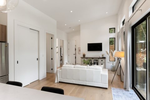 Bright modern living room with white leather sofa, large windows, and minimalist decor.