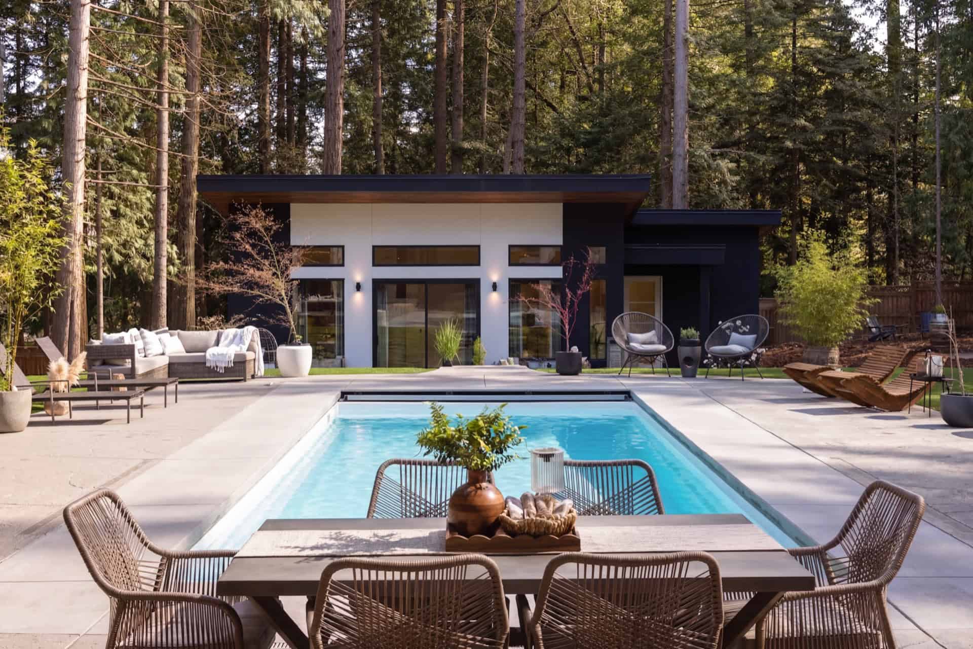 Outdoor pool area with modern backyard living space and wooden deck, surrounded by trees.