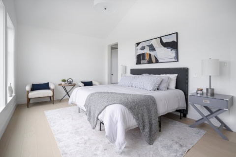 Bright modern bedroom with a gray upholstered bed, matching nightstands, abstract wall art, and a he.