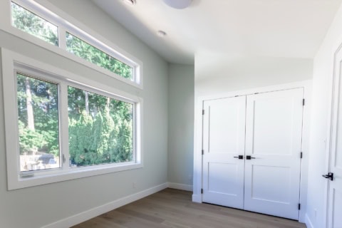 Bright bedroom with large windows and white closet doors in a modern Victoria home.
