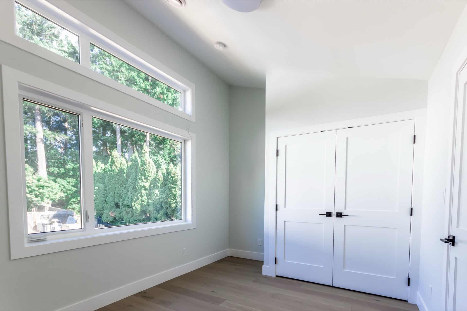 Bright bedroom with large windows and white closet doors in a modern Victoria home.