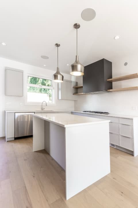 Modern white kitchen with island, pendant lights, and stainless steel appliances in Victoria BC home.