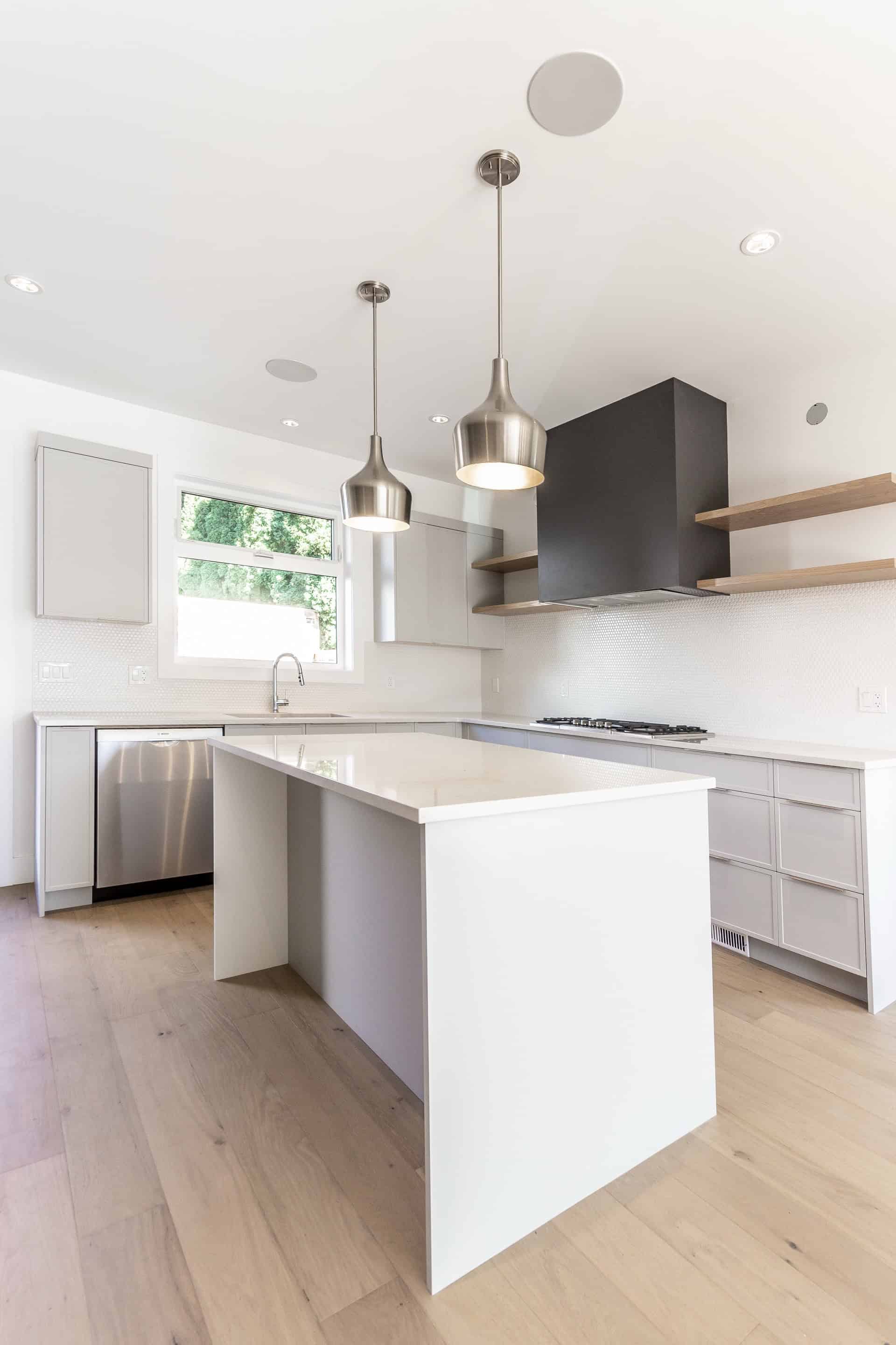 Modern white kitchen with island, pendant lights, and stainless steel appliances in Victoria BC home.