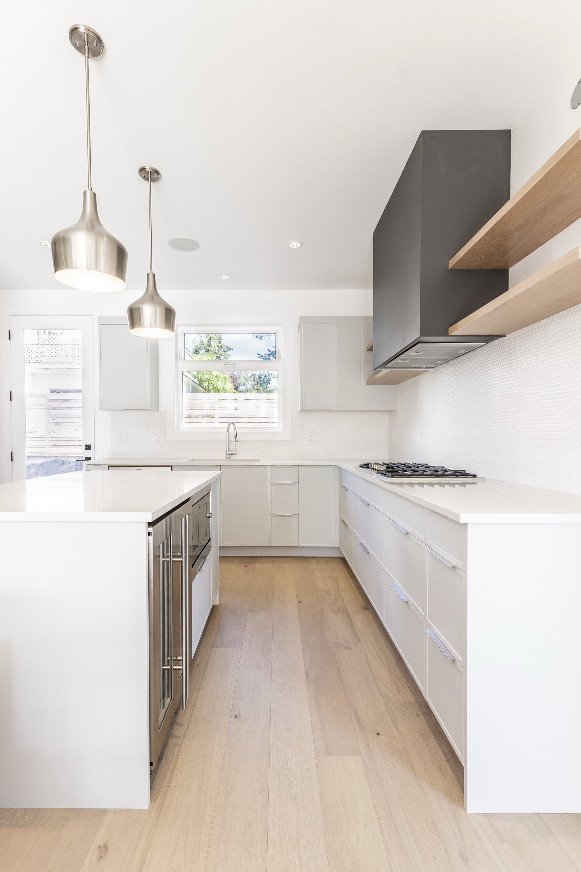 Bright white modern kitchen with island, pendant lights, and stainless steel appliances.