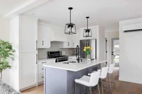 Modern white kitchen with island, pendant lights, and bar seating in Victoria BC home.