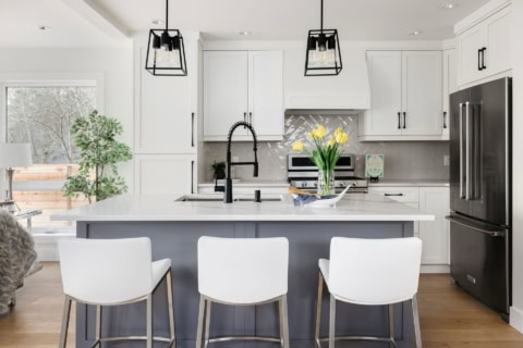 Modern white kitchen featuring island with sink, pendant lights, and yellow flowers.