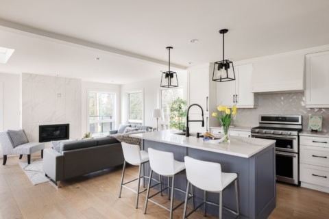 Open-plan kitchen with large island, white cabinets, stainless steel appliances and pendant lights.
