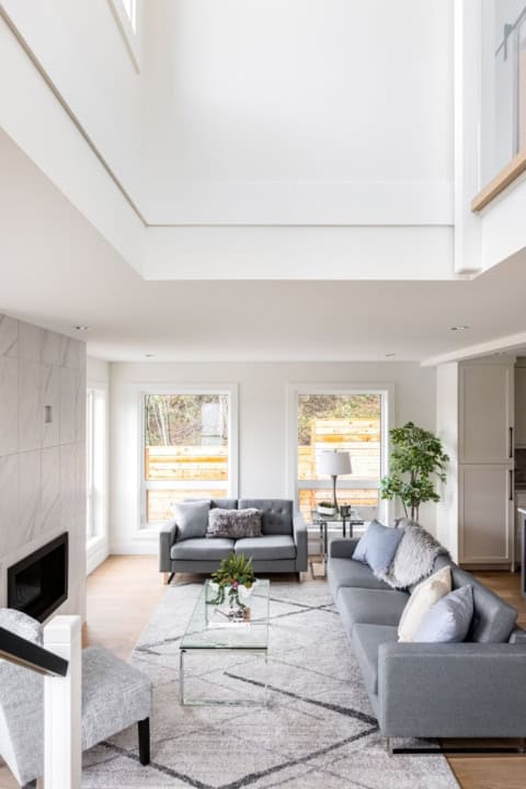 Open concept living room with grey sofas, glass coffee table, and skylight in a bright white modern.