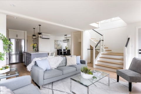Bright open-concept living room with grey furniture, glass coffee table, and staircase at Arbutus R​.