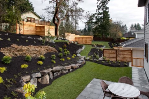 Backyard landscape with tiered rock retaining walls, fresh mulch, and seating area under a wooden-st.