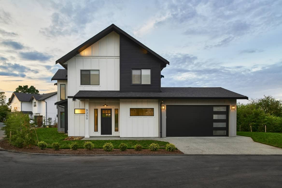 Modern two-story home with white and dark siding, attached garage, and landscaped front yard.