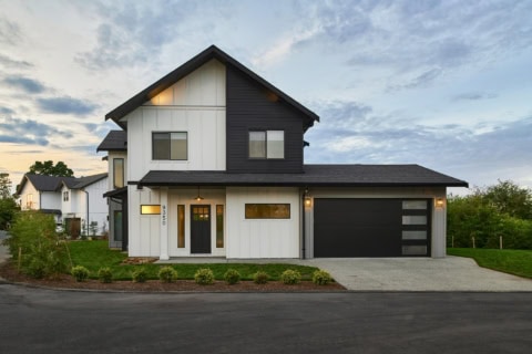 Modern two-story home with white and dark siding, attached garage, and landscaped front yard.