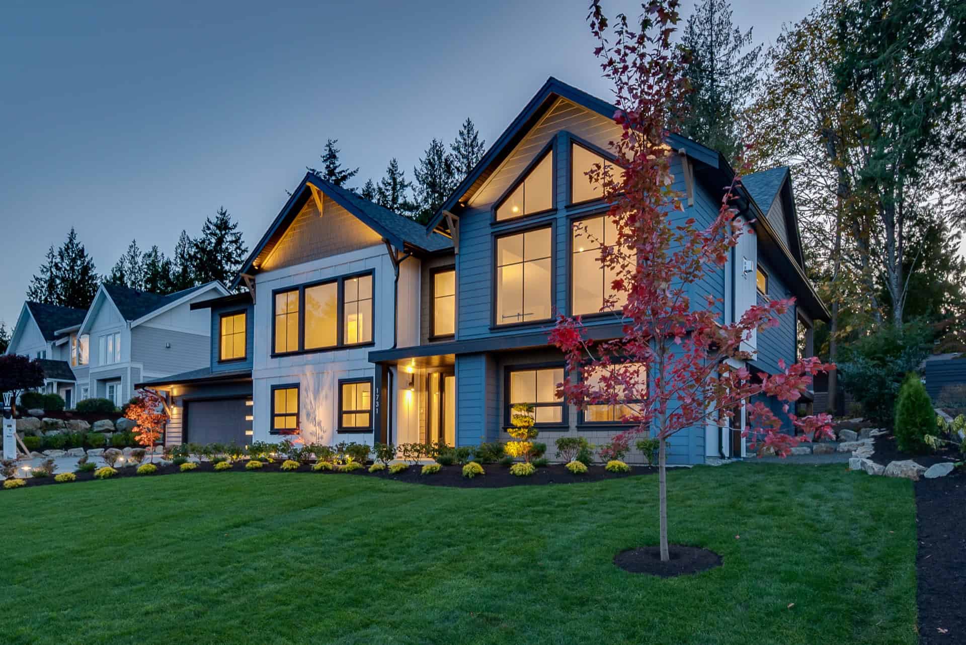 Modern Victoria BC custom home with illuminated interior through large windows and landscaped front.