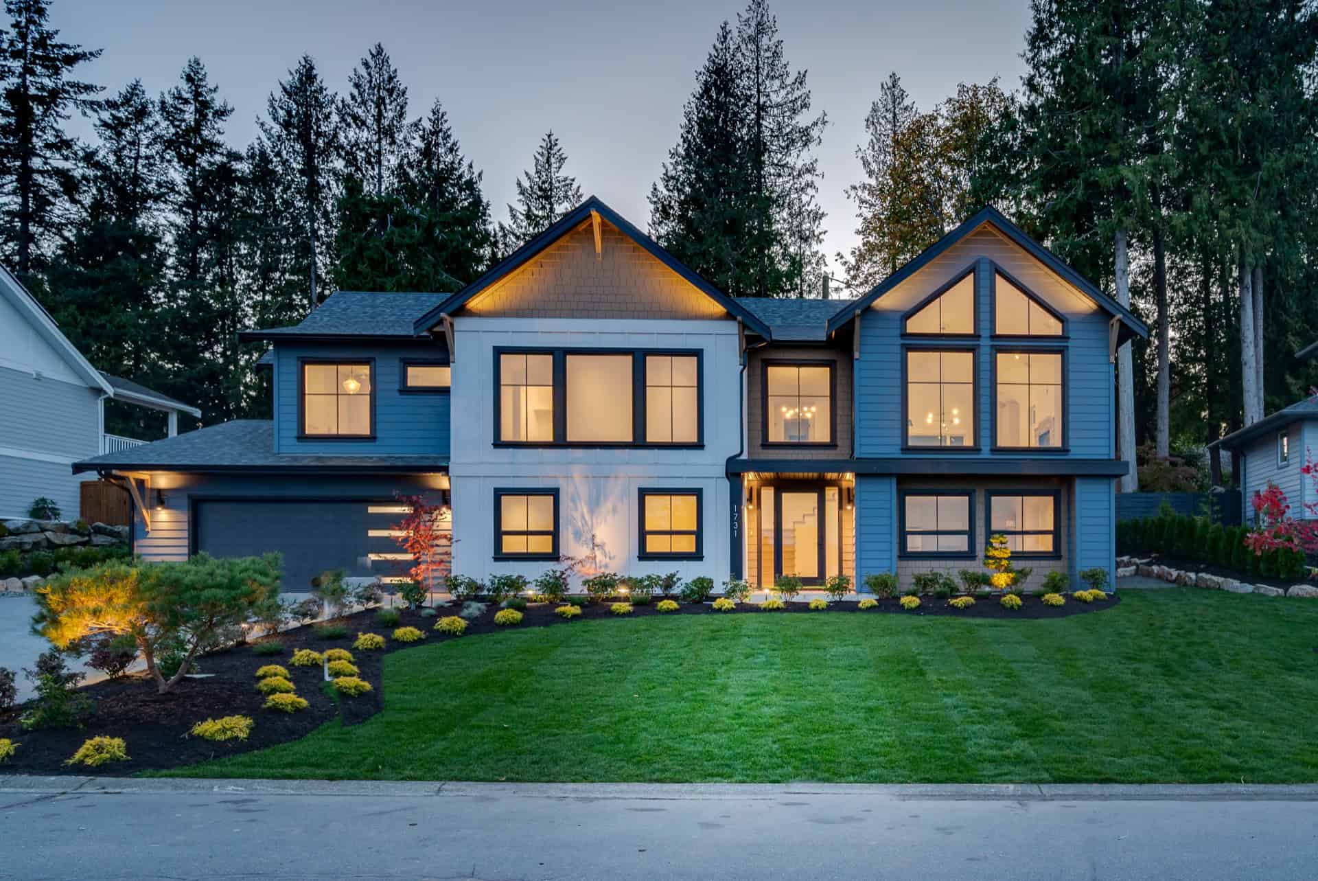 Elegant modern two-story home with manicured lawn and warm exterior lighting.
