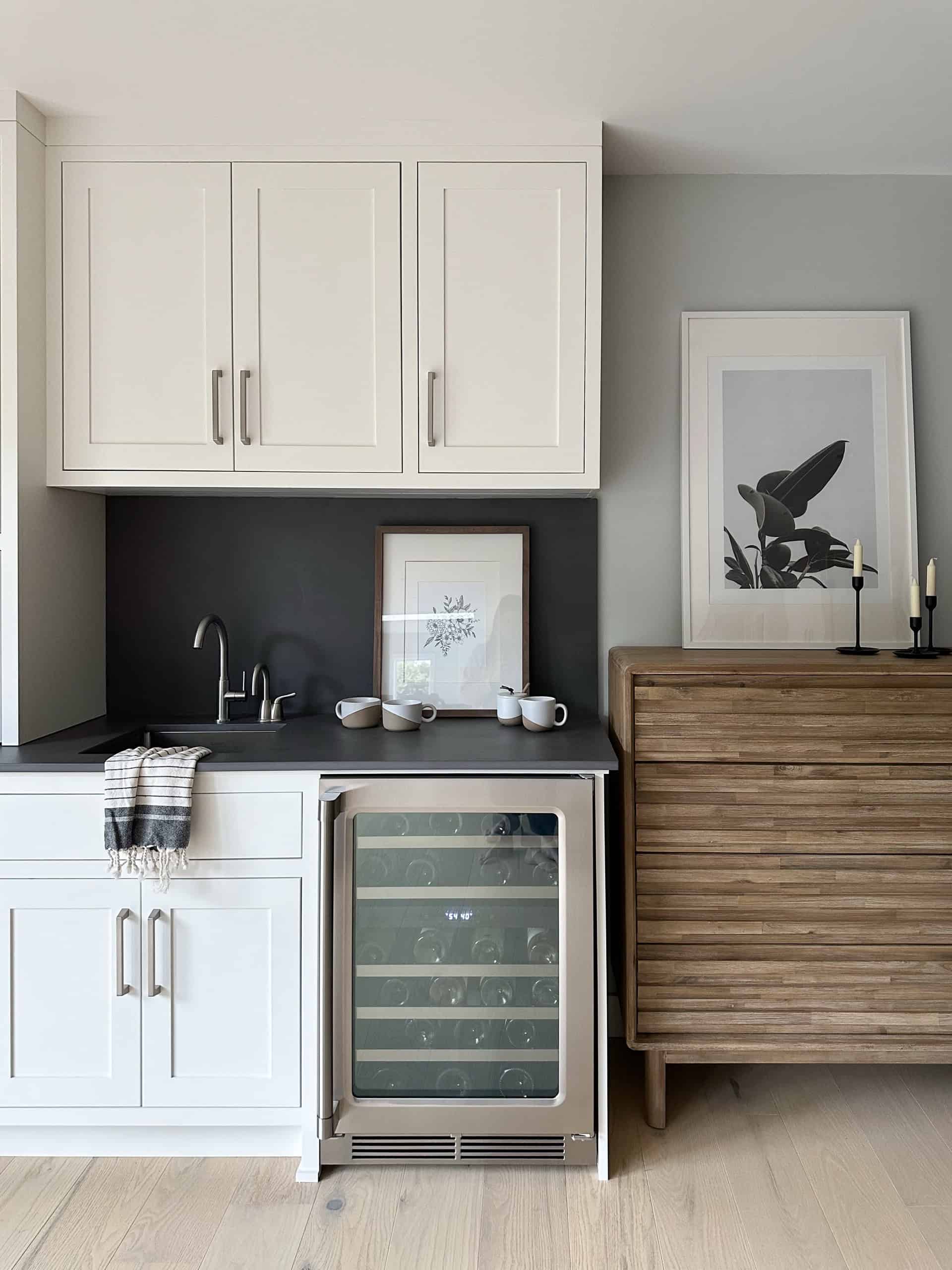 Modern compact kitchen with white cabinets, wine cooler, and wooden sideboard in a light-filled room.