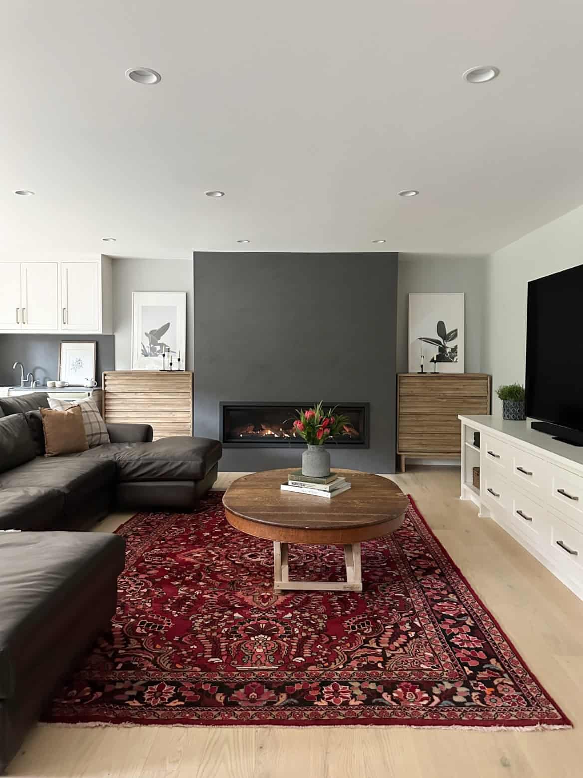 Modern living room with fireplace, dark accent wall, and red patterned rug in a bright open-plan.