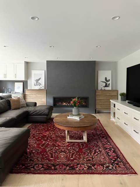 Modern living room with fireplace, dark accent wall, and red patterned rug in a bright open-plan.